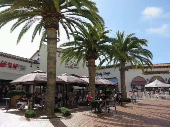 White Spanish-style buildings in an outlet mall, with views of hills from the parking lot.