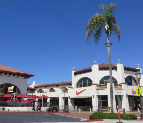 White Spanish-style buildings in an outlet mall, with views of hills from the parking lot.