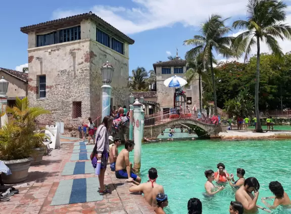 Unique spring-fed historical pool with Venetian-style buildings, bridge, striped posts, waterfall, caves, palms, and banyan tree. Glorious!
