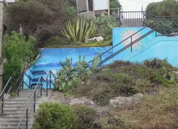 Fun beach with many spots to explore, including rock pools, a walking path with flowers above the sea, basketball courts, a playground, and a lawn by the beach.