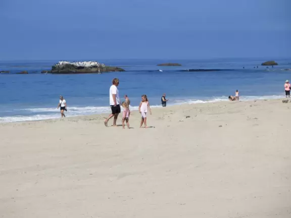 Fun beach with many spots to explore, including rock pools, a walking path with flowers above the sea, basketball courts, a playground, and a lawn by the beach.