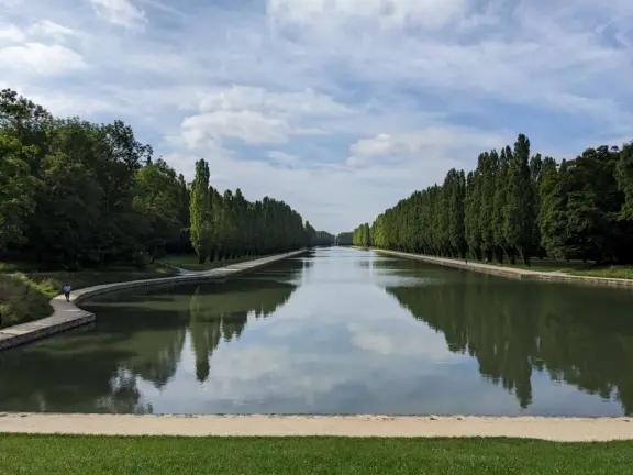 A beautiful park with a grand canal, an impressively high fountain, flower beds, a chateau, and the loveliest trees.
