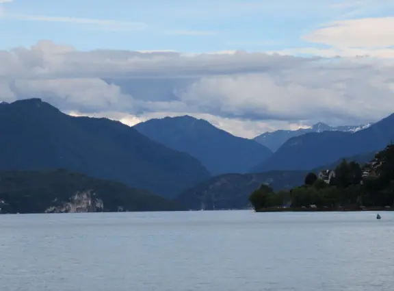 Lakeside park like an arboretum, with tall amazing trees from around the world, statues, modern art sculptures, stunning mountain views, ironwork lovers bridge, and promenade along the blue-green lake.