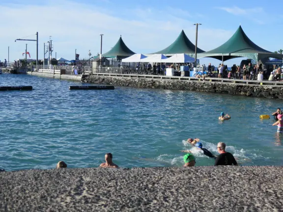 Pier with crystal clear water and views of the church steeple and high mountains backing the bay. Calm cove with Hawaiian hei'au out in the water.