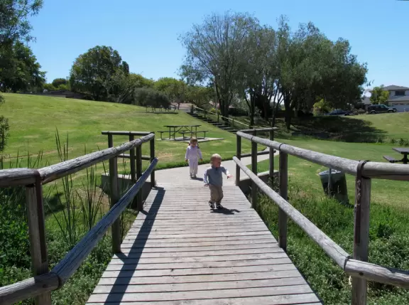 Neighborhood park shaped like a bowl with playground, forest, wooden bridges, and winding paths.