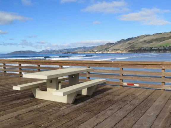 Gorgeous spot with wide pier, surfers carving the waves, whale playground, wide open attractive plaza, Pismo Beach selfie sign, and wooden promenade with views of the hills and sea.