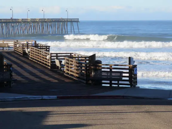 Gorgeous spot with wide pier, surfers carving the waves, whale playground, wide open attractive plaza, Pismo Beach selfie sign, and wooden promenade with views of the hills and sea.