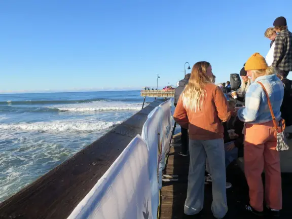 Gorgeous spot with wide pier, surfers carving the waves, whale playground, wide open attractive plaza, Pismo Beach selfie sign, and wooden promenade with views of the hills and sea.