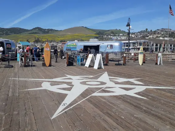 Gorgeous spot with wide pier, surfers carving the waves, whale playground, wide open attractive plaza, Pismo Beach selfie sign, and wooden promenade with views of the hills and sea.
