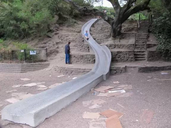 A playground with giant concrete slide, in a bowl surrounded by forest in the hills above Berkeley.