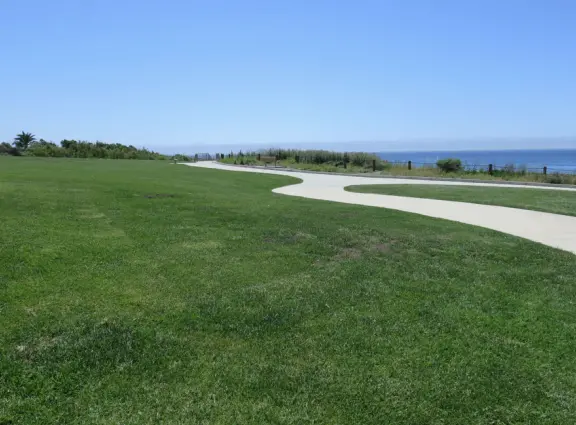 Stretch of grass with a paved walkway, flower beds, wonderful ocean views to Avila Beach, and monterey cypress trees.