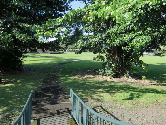 Beautiful statue backed by trees, with fruit and flower offerings below it. Huge lawn, narrow paths, picnic tables, and pedestrian bridge to Wailoa River State Park.