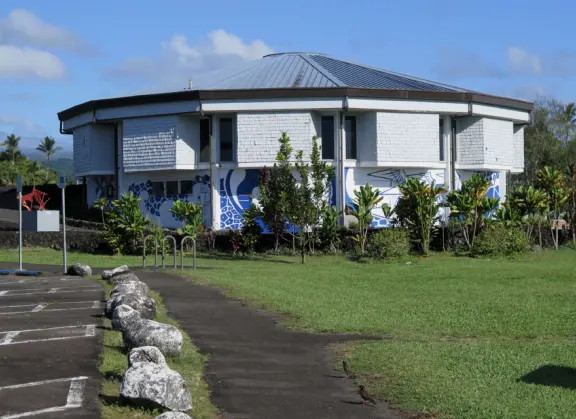 Beautiful statue backed by trees, with fruit and flower offerings below it. Huge lawn, narrow paths, picnic tables, and pedestrian bridge to Wailoa River State Park.