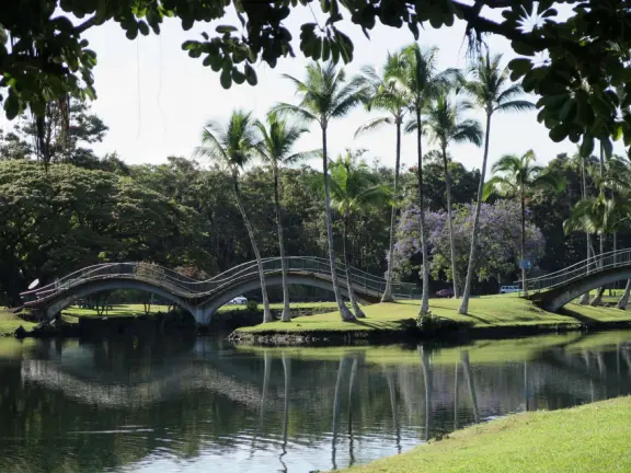 Beautiful statue backed by trees, with fruit and flower offerings below it. Huge lawn, narrow paths, picnic tables, and pedestrian bridge to Wailoa River State Park.
