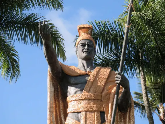 Beautiful statue backed by trees, with fruit and flower offerings below it. Huge lawn, narrow paths, picnic tables, and pedestrian bridge to Wailoa River State Park.
