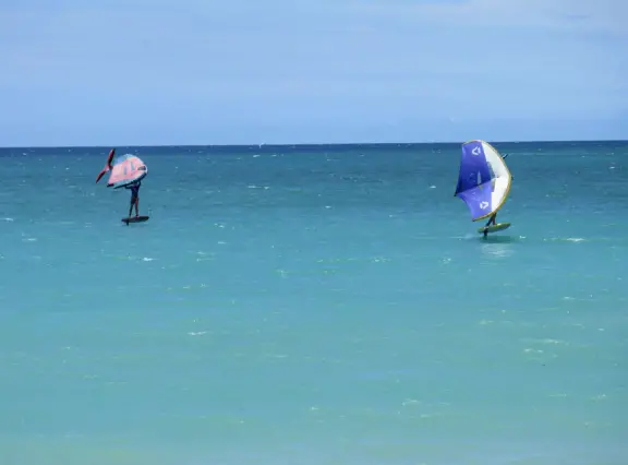 An incredibly beautiful beach with technicolor water, white sand strewn with coral, and colorful kite surfers zooming by, all framed by gorgeous mountains.
