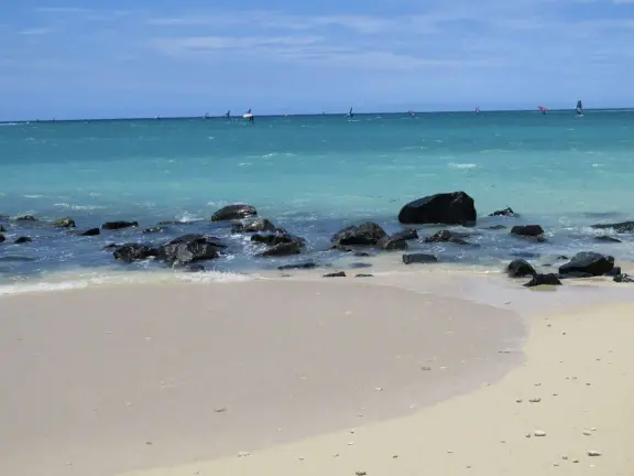 An incredibly beautiful beach with technicolor water, white sand strewn with coral, and colorful kite surfers zooming by, all framed by gorgeous mountains.