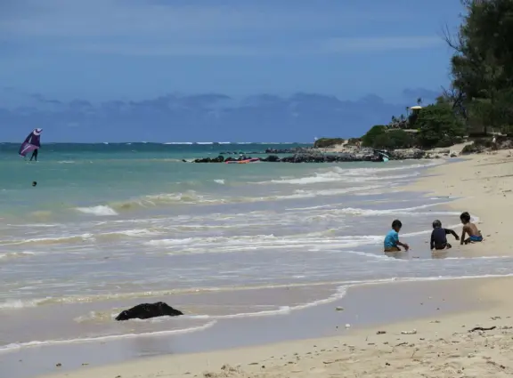 An incredibly beautiful beach with technicolor water, white sand strewn with coral, and colorful kite surfers zooming by, all framed by gorgeous mountains.
