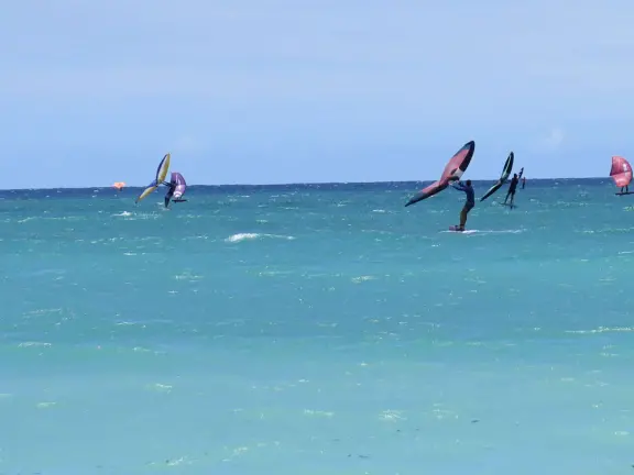An incredibly beautiful beach with technicolor water, white sand strewn with coral, and colorful kite surfers zooming by, all framed by gorgeous mountains.