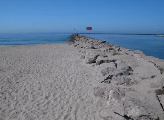 White sandy beach with rock jetty, beach houses, and boardwalk by the harbor.
