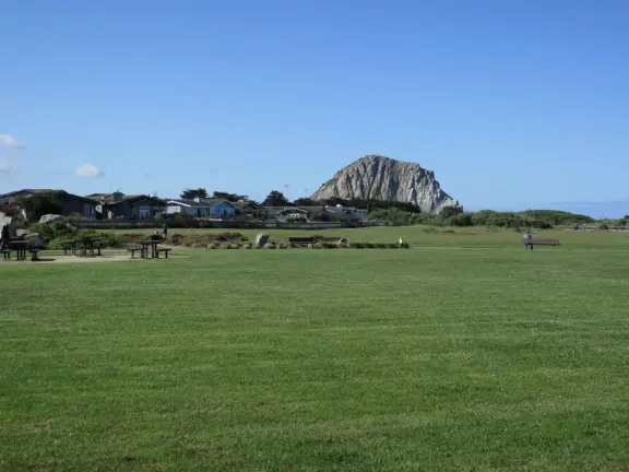 Wide open park behind the dunes in Morro Bay, with play structure with sand floor, and huge lawn with winding paths for tricycling.