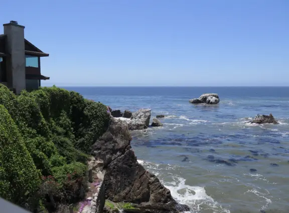 Walkway with benches above the ocean, and steps that lead down to tide pools and beach with reddish-hued sand and lovely cliffs.