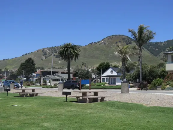 Walkway with benches above the ocean, and steps that lead down to tide pools and beach with reddish-hued sand and lovely cliffs.