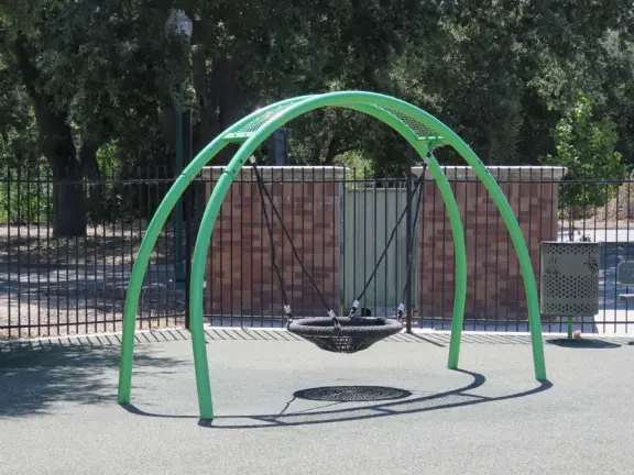 Large, fenced, spread-out playground with treehouse structure, varied swings in the shade, dragonfly seesaw, egg seat, disc swing, and spinner.