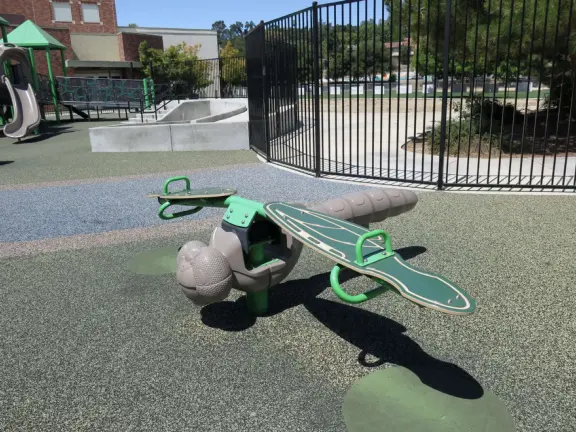 Large, fenced, spread-out playground with treehouse structure, varied swings in the shade, dragonfly seesaw, egg seat, disc swing, and spinner.