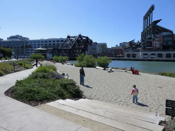 Modern area, also called Mission Bay, with French bakery, waterfront bike path that connects to Embarcadero, and views across to Oracle Park stadium and the Bay Bridge.