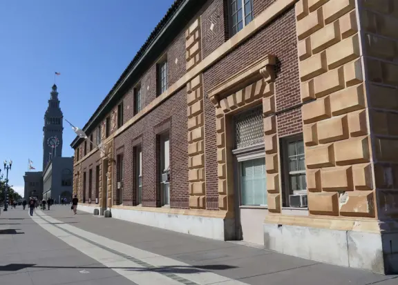 Wide, 3-mile-long walkway on the waterfront with blue lampposts, canary palms, lawns, modern sculptures, and views of the Bay Bridge. Find ferries, restaurants, touristy shops, and museums.