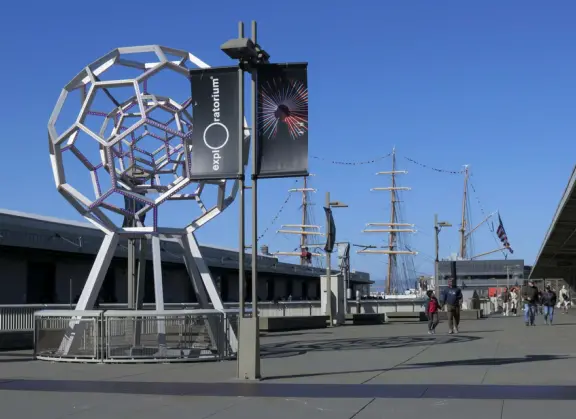 Wide, 3-mile-long walkway on the waterfront with blue lampposts, canary palms, lawns, modern sculptures, and views of the Bay Bridge. Find ferries, restaurants, touristy shops, and museums.
