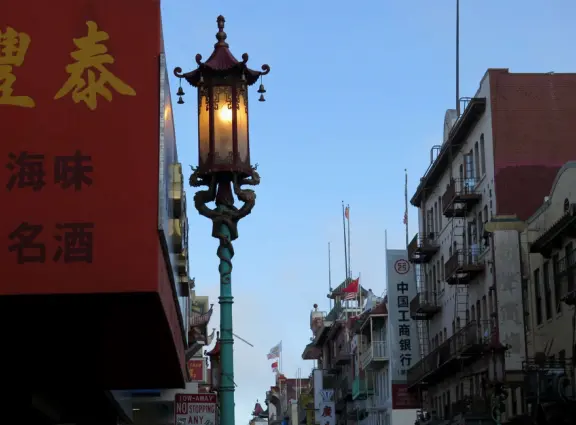 Street with red lanterns with gold tassles, whimsical lampposts, and storefronts that swoop up in the corners.