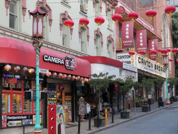 Street with red lanterns with gold tassles, whimsical lampposts, and storefronts that swoop up in the corners.