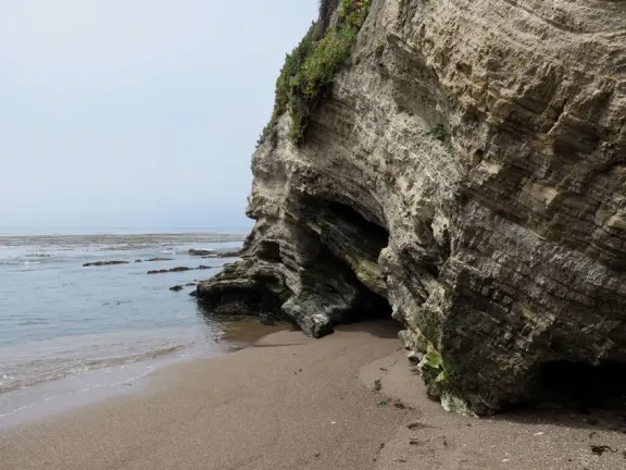 Walkway with benches above the ocean, and steps that lead down to tide pools and beach with reddish-hued sand and lovely cliffs.