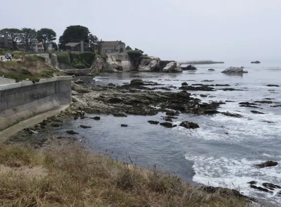 Walkway with benches above the ocean, and steps that lead down to tide pools and beach with reddish-hued sand and lovely cliffs.