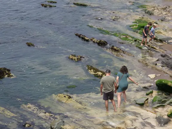 Walkway with benches above the ocean, and steps that lead down to tide pools and beach with reddish-hued sand and lovely cliffs.