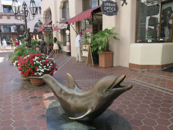 A Spanish paseo and courtyard with archways, little lights, flags, murals, lifelike statues, and fountains. At night, a magical spot!