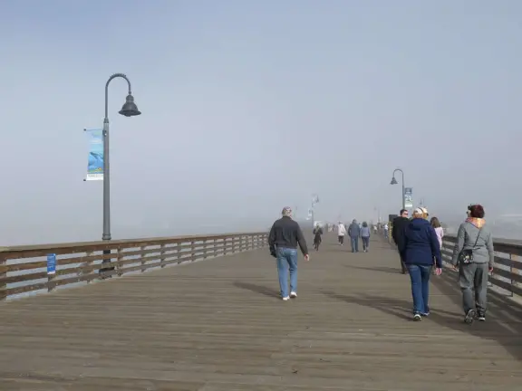 Gorgeous spot with wide pier, surfers carving the waves, whale playground, wide open attractive plaza, Pismo Beach selfie sign, and wooden promenade with views of the hills and sea.