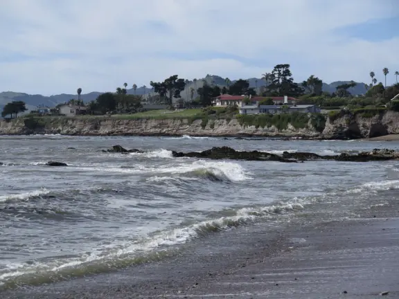 Walkway with benches above the ocean, and steps that lead down to tide pools and beach with reddish-hued sand and lovely cliffs.