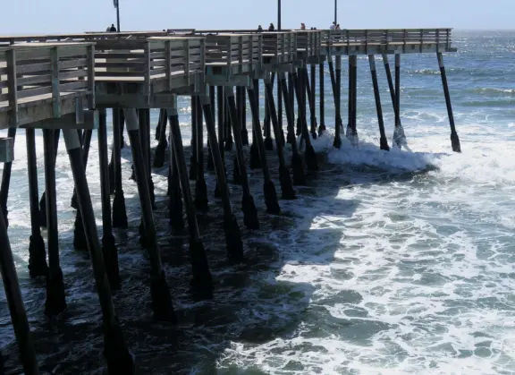 Gorgeous spot with wide pier, surfers carving the waves, whale playground, wide open attractive plaza, Pismo Beach selfie sign, and wooden promenade with views of the hills and sea.