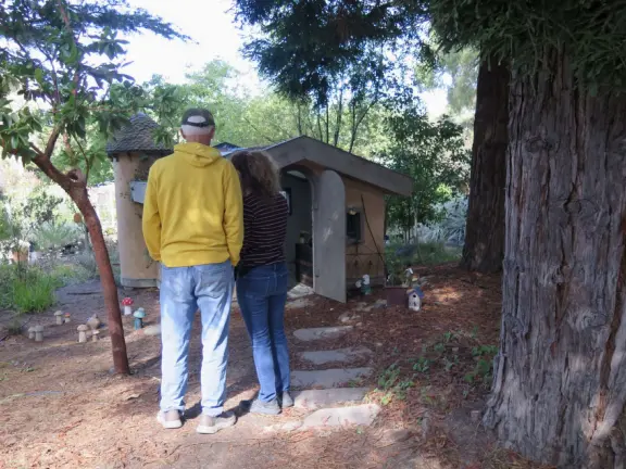 A couple stand in the redwood grove checking out the German-style cottage with turret.