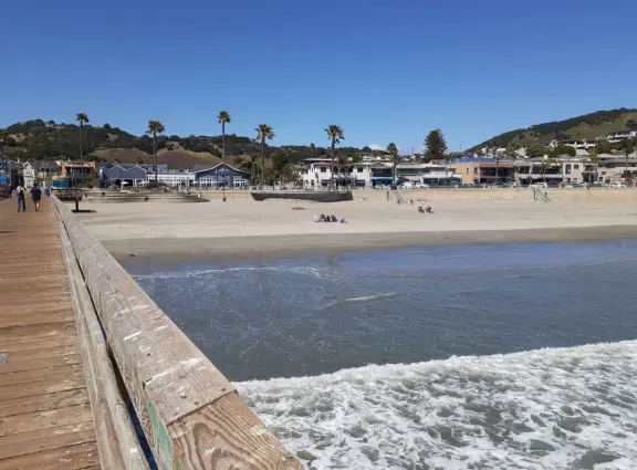 Gorgeous street of colorful, attractive buildings overlooking a beach with stunning headlands. Wooden pier.