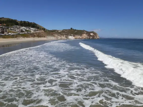 Gorgeous street of colorful, attractive buildings overlooking a beach with stunning headlands. Wooden pier.