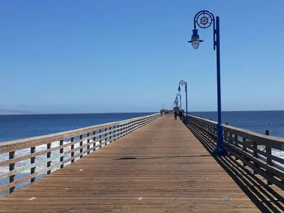 Gorgeous street of colorful, attractive buildings overlooking a beach with stunning headlands. Wooden pier.