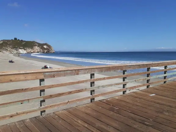 Gorgeous street of colorful, attractive buildings overlooking a beach with stunning headlands. Wooden pier.