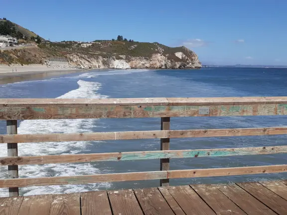 Gorgeous street of colorful, attractive buildings overlooking a beach with stunning headlands. Wooden pier.