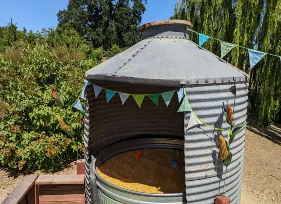 Pristine farm by a hill covered in bright foliage, with oil and vinegar tasting, honey tasting, u-pick, farm store, and adorable kids area with goats, chickens, rabbits, and colorful play areas.