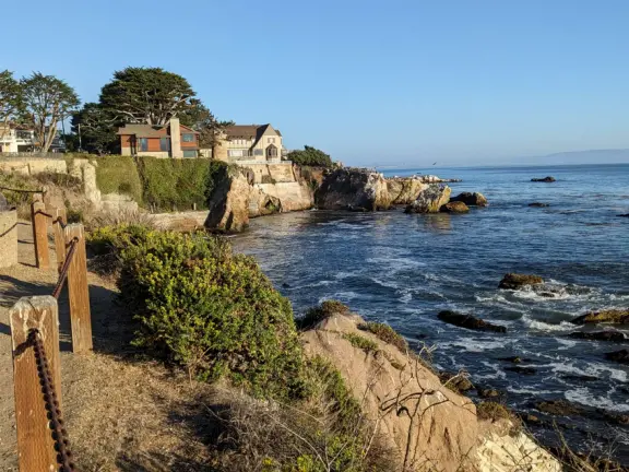 Walkway with benches above the ocean, and steps that lead down to tide pools and beach with reddish-hued sand and lovely cliffs.