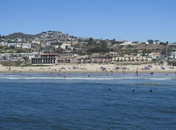 Gorgeous spot with wide pier, surfers carving the waves, whale playground, wide open attractive plaza, Pismo Beach selfie sign, and wooden promenade with views of the hills and sea.